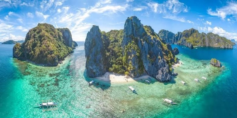 A happy Indian family is pictured smiling on a stunning white sand beach in the Philippines, with clear blue water and lush green palm trees in the background, suggesting an easy and joyful vacation thanks to the new visa policy.