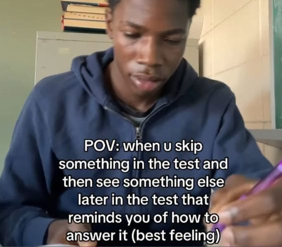 A young person wearing a blue hoodie is sitting at a desk, holding a pen and looking thoughtful. In the background, there are books stacked on a shelf and a green chalkboard. Text overlay on the image reads: "POV: when u skip something in the test and then see something else later in the test that reminds you of how to answer it (best feeling)."
