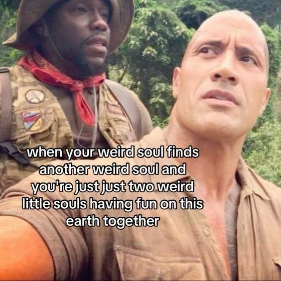 Two people are depicted in an outdoor setting with greenery in the background. One wears a safari hat, red bandana, and camouflage outfit, while the other is in a beige shirt, looking surprised. Text overlay reads: "when your weird soul finds another weird soul and you're just two weird little souls having fun on this earth together." The Rock meme 