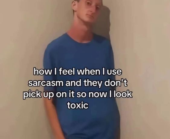 A person wearing a blue t-shirt stands against a plain beige wall, looking slightly awkward. The text overlay reads: "how I feel when I use sarcasm and they don't pick up on it so now I look toxic."