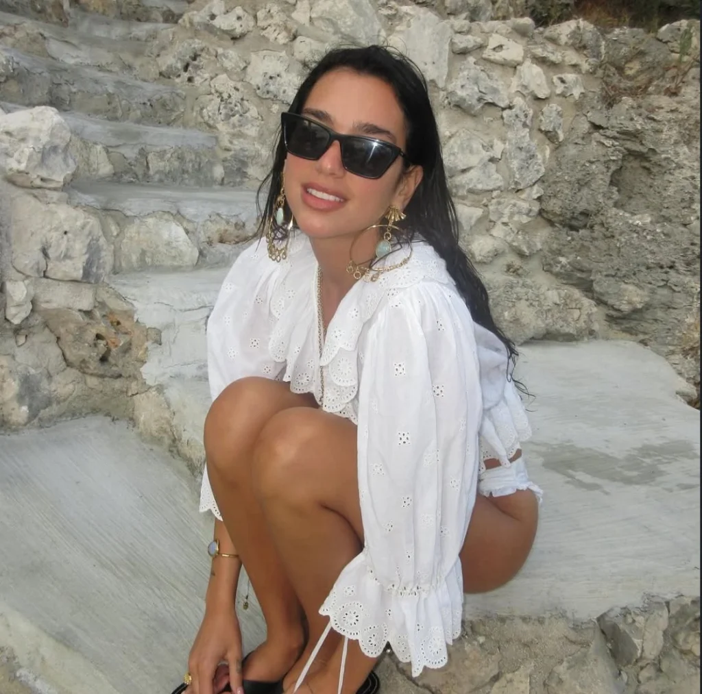 Dua Lipa smiles brightly wearing a chic outfit, showcasing her signature modern pop star style on Instagram.