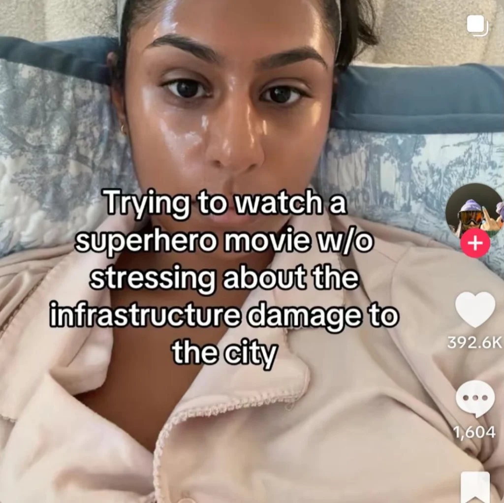 A viral meme shows a woman lying in bed, humorously stressing over fictional infrastructure damage during superhero films instead of enjoying the battles.