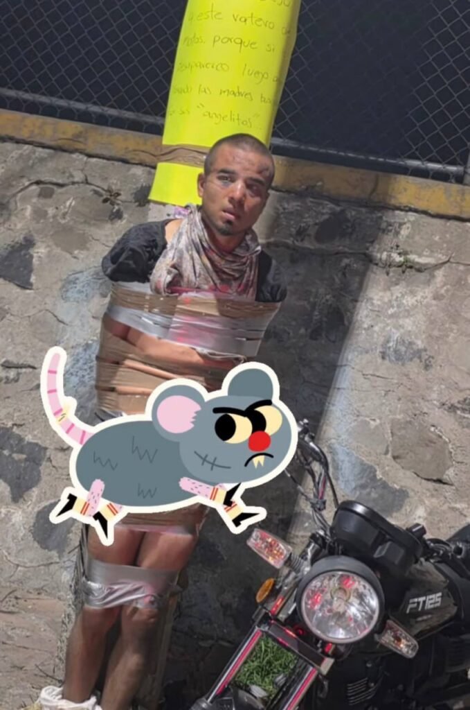 Close-up photo of suspected motorbike thief restrained with heavy-duty tape against wooden lamppost during daytime, showing vigilante justice method used by Mexican Batman