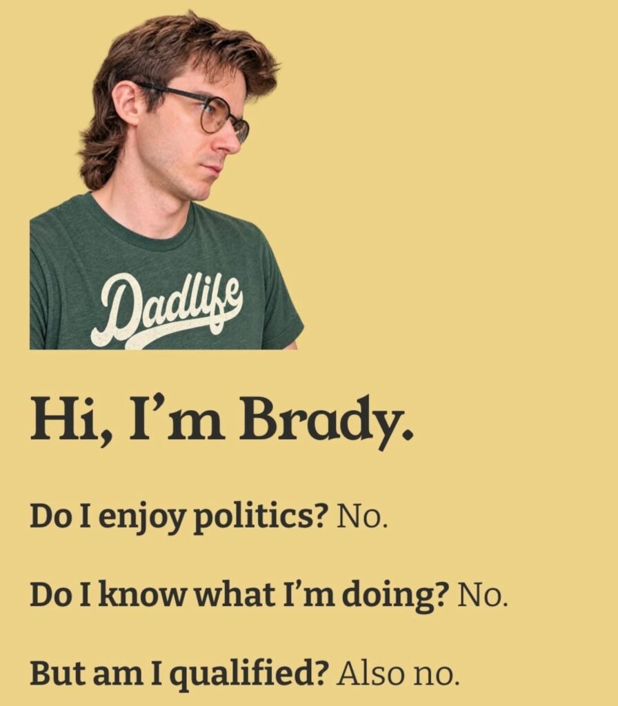 Brady Rogers, Kelowna city council winner, standing beside a humorous campaign sign about not wanting to do politics